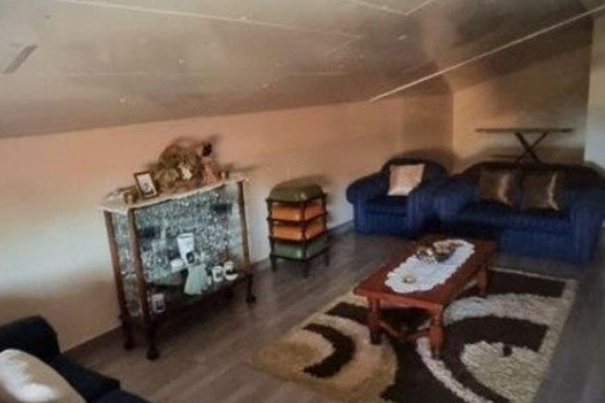 A living room area featuring a sloped ceiling and laminate flooring, requiring cosmetic updates to improve the overall finish and aesthetic appeal.