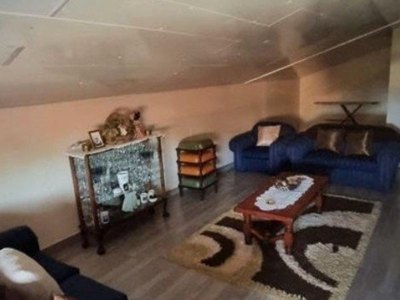 A living room area featuring a sloped ceiling and laminate flooring, requiring cosmetic updates to improve the overall finish and aesthetic appeal.