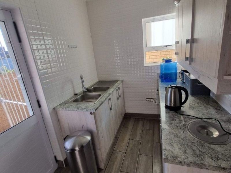 A functional scullery featuring granite countertops, double bowl sink, built-in cabinetry, and durable wood-look floor tiles with direct access to the exterior.