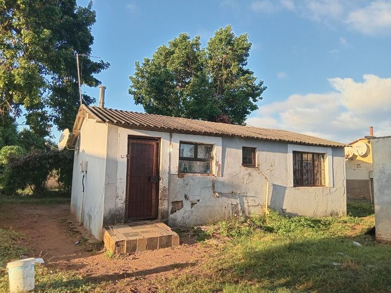 A detached single-story structure featuring masonry walls, a corrugated roof, and steel window frames, showing significant signs of exterior wear and plaster deterioration.