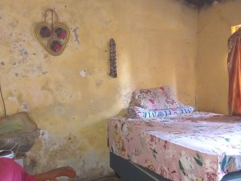 A bedroom featuring exposed roof rafters and corrugated sheeting, requiring significant wall repairs and cosmetic renovation to improve the overall condition.