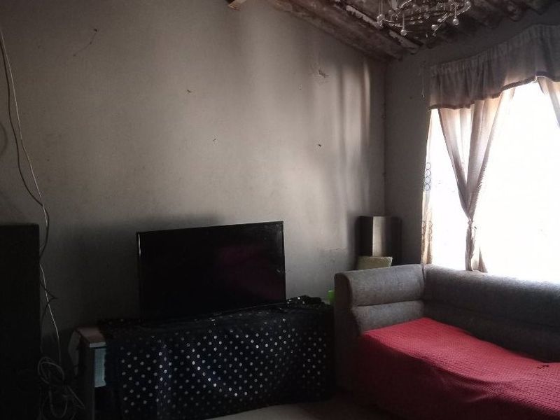 A living room featuring tiled flooring, an exposed corrugated roof structure, and a chandelier, requiring significant cosmetic updates and ceiling finishing.