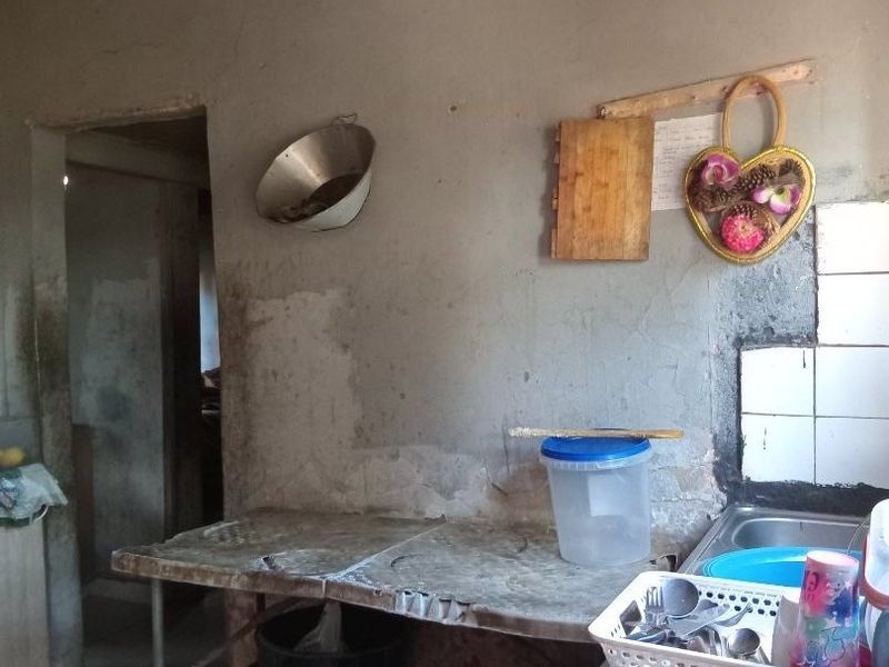 A basic kitchen area featuring a stainless steel sink, tiled splashback, and tiled flooring, requiring significant renovation and finishing to improve the space.
