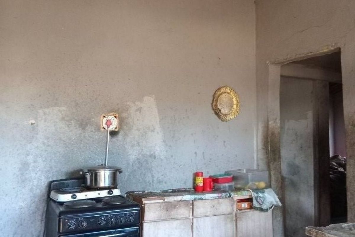 A basic kitchen area featuring a freestanding stove, base cabinetry, and tiled flooring, requiring significant renovation to improve the wall finishes and overall condition.