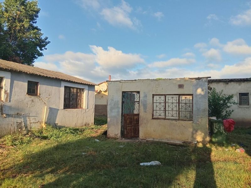 Rear view of the property showing multiple outbuildings with weathered plaster finishes, security bars on windows, and corrugated roofing in need of maintenance.