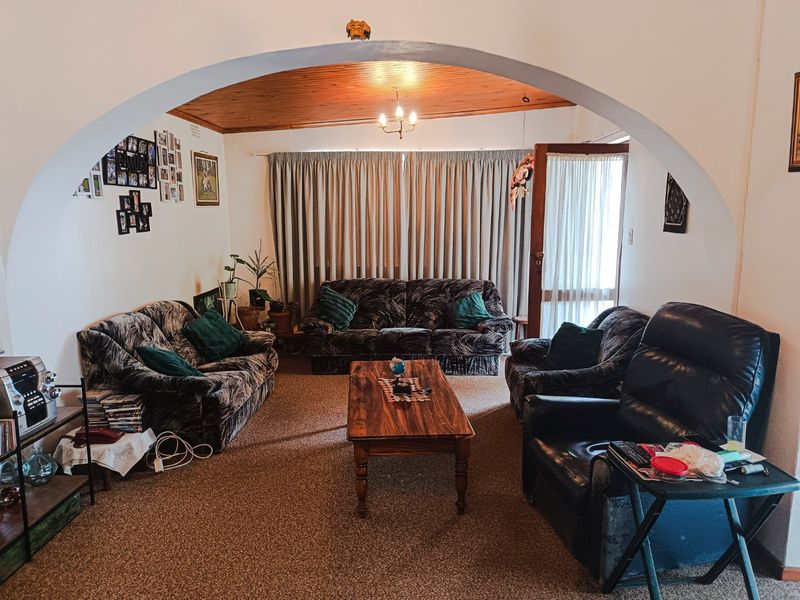 A cozy living room featuring a distinctive arched entryway, warm timber ceiling, and direct access to the outdoors through a sliding glass door.