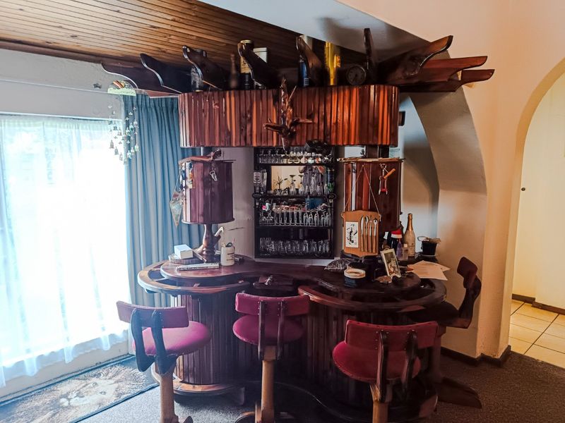 A dedicated home bar area featuring a built-in wooden bar counter, integrated shelving, and a timber-clad ceiling.