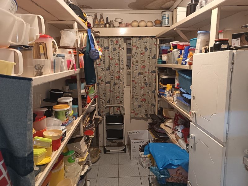 A functional scullery or pantry area featuring extensive built-in shelving and tiled flooring, currently used for storage.