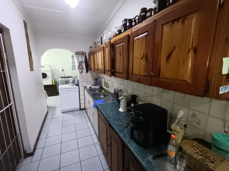 A functional scullery area featuring wooden cabinetry, a double basin sink, and tiled splashbacks, providing additional prep and wash-up space adjacent to the kitchen.