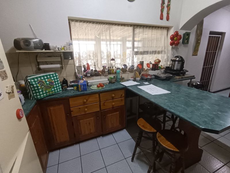 A dated kitchen featuring wooden cabinetry, laminate countertops, and tiled flooring, offering potential for a modern renovation.
