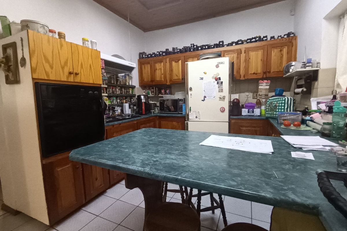 A functional kitchen featuring traditional wooden cabinetry, laminate countertops, built-in oven, and hob, with tiled flooring and a timber ceiling.