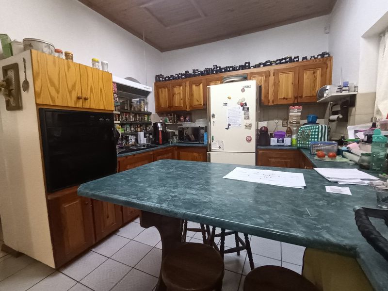A functional kitchen featuring traditional wooden cabinetry, laminate countertops, built-in oven, and hob, with tiled flooring and a timber ceiling.