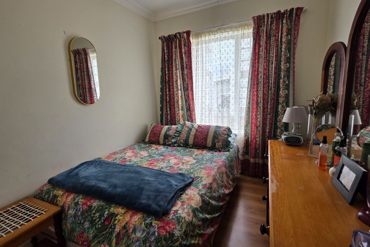 A cozy bedroom featuring laminate flooring and classic window treatments, offering a functional space with potential for modern updates.