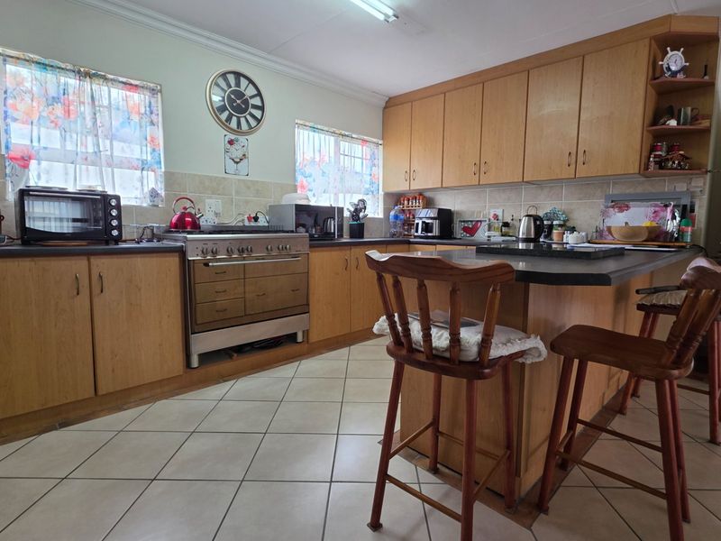 A functional kitchen featuring wooden cabinetry, tiled flooring, a central island, and a built-in oven and hob setup.