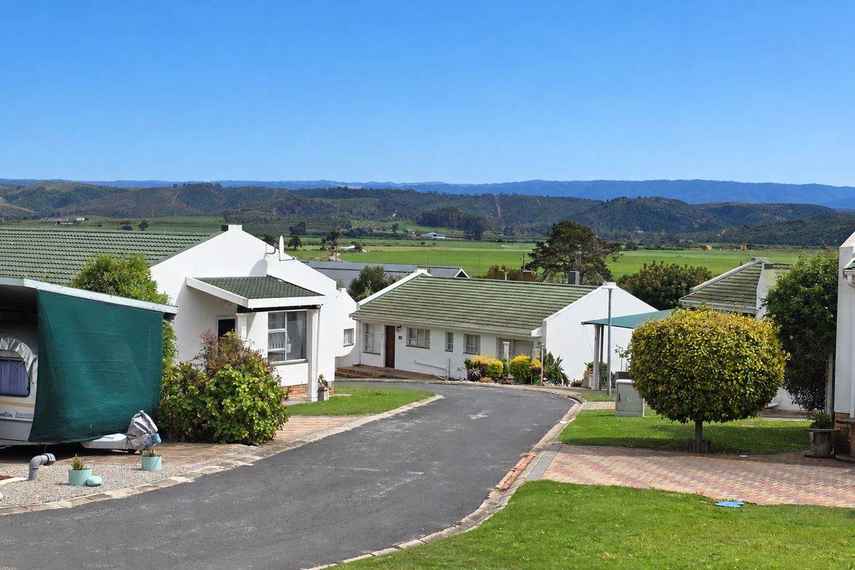 A view of the rear exterior of the property, featuring a paved driveway, landscaped garden, and tiled roof structures with scenic mountain views.