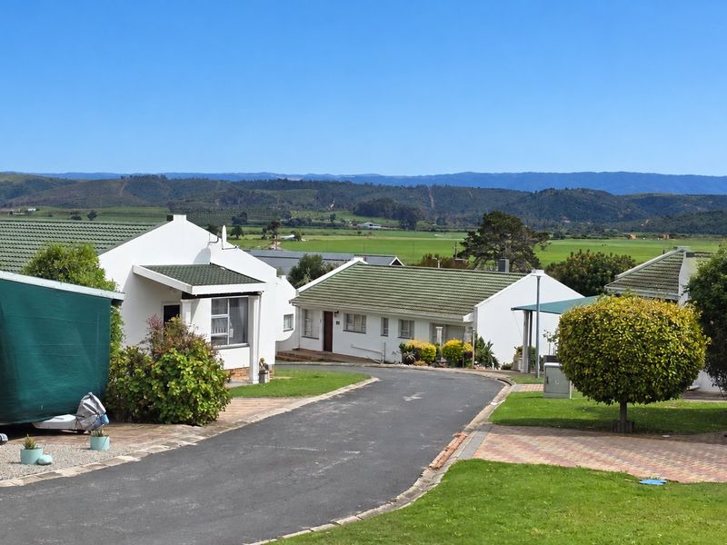 A view of the rear exterior of the property, featuring a paved driveway, landscaped garden, and tiled roof structures with scenic mountain views.