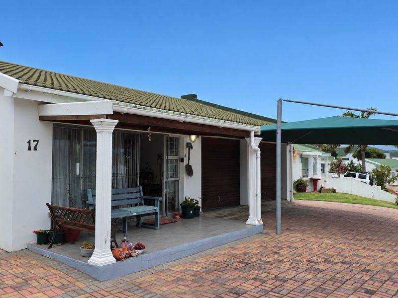 Front elevation of a single-story house featuring a covered patio with decorative columns, a paved driveway, and a shade sail carport.