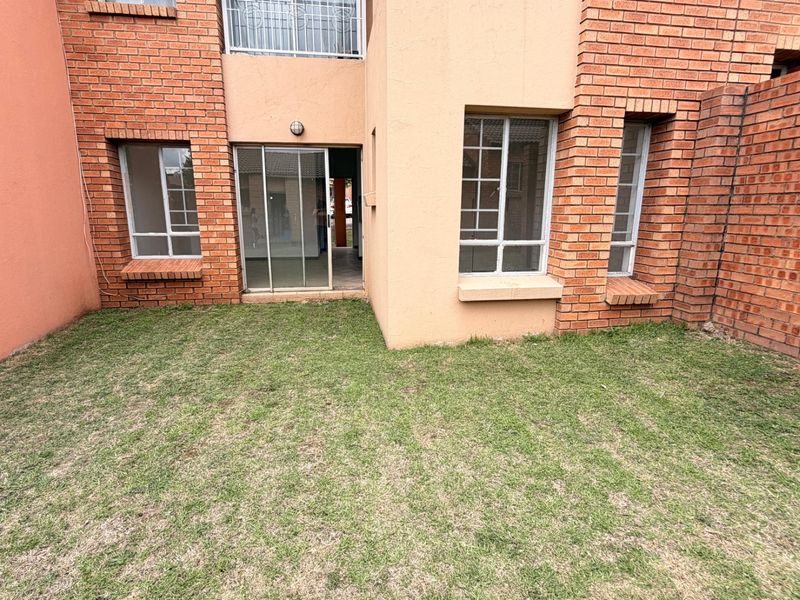 A rear view of the apartment featuring a private lawn area, brick facade, and sliding door access to the interior living space.