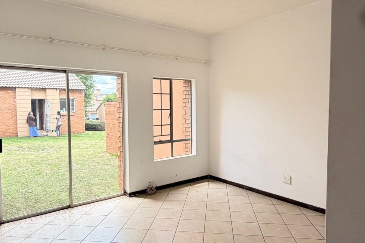 An empty living room featuring tiled flooring, a sliding glass door providing garden access, and a steel frame window, offering a blank canvas for renovation.