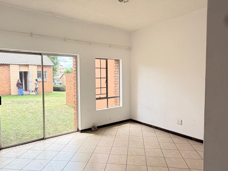 An empty living room featuring tiled flooring, a sliding glass door providing garden access, and a steel frame window, offering a blank canvas for renovation.