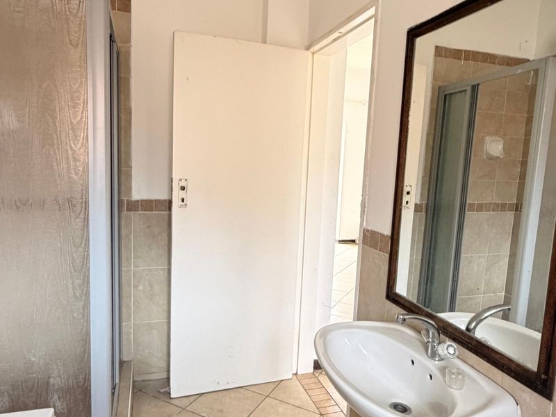 A functional bathroom featuring a pedestal basin, shower enclosure, and neutral wall and floor tiling, offering potential for a modern renovation.