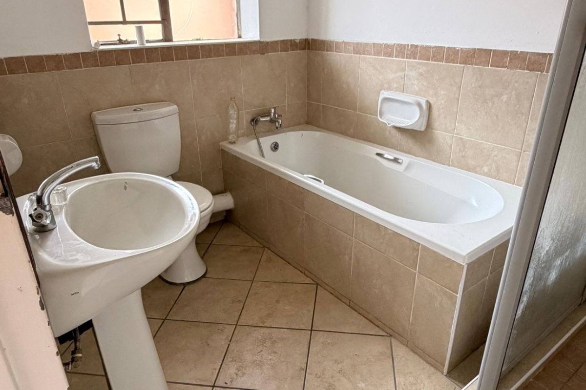 A dated bathroom featuring a pedestal basin, toilet, built-in bathtub, and separate shower enclosure with neutral ceramic tiling throughout.