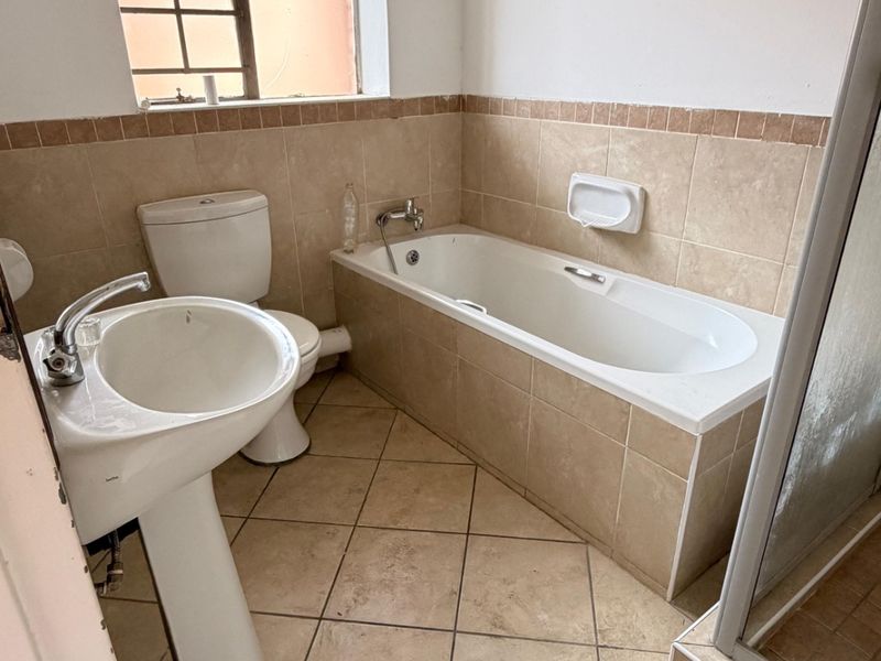 A dated bathroom featuring a pedestal basin, toilet, built-in bathtub, and separate shower enclosure with neutral ceramic tiling throughout.