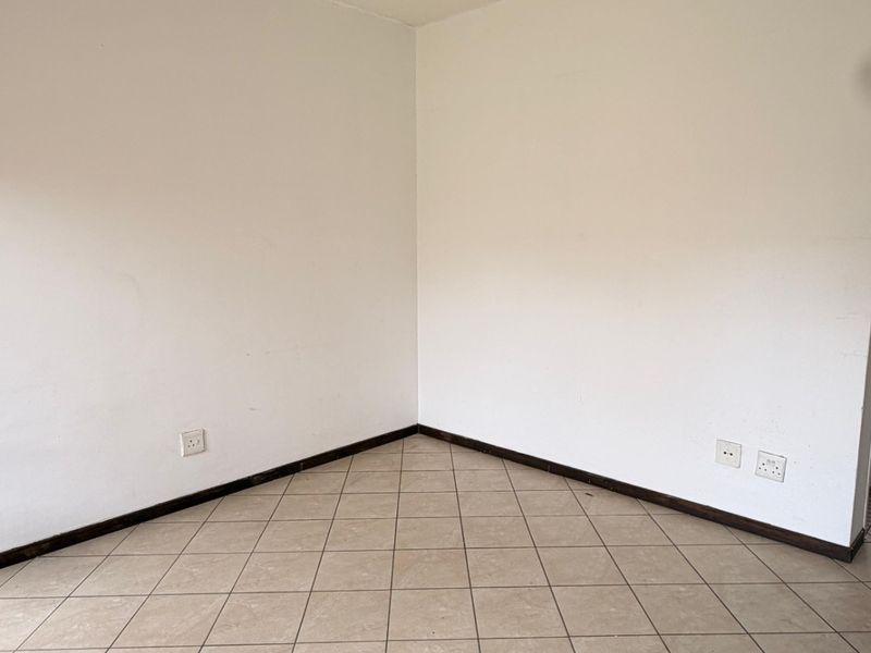 An empty living room corner featuring neutral floor tiles, white walls, and standard electrical fixtures, providing a blank canvas for interior design.
