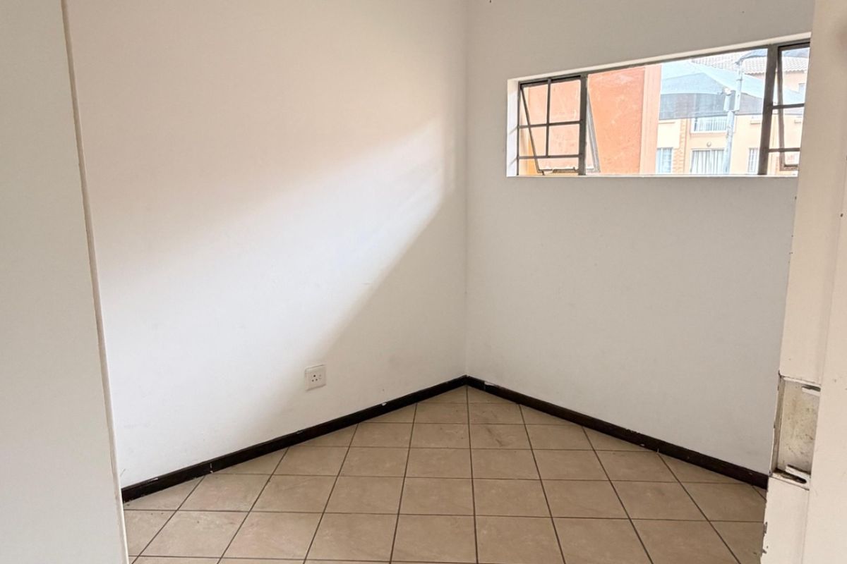 An empty bedroom featuring tiled flooring, a ceiling light fixture, and a horizontal window, providing a blank canvas for potential interior design updates.