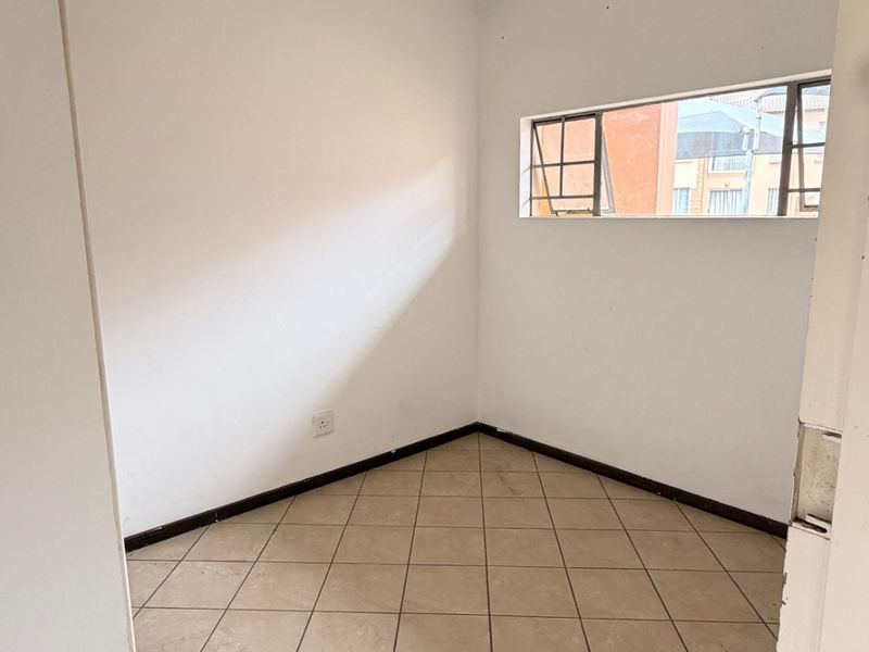 An empty bedroom featuring tiled flooring, a ceiling light fixture, and a horizontal window, providing a blank canvas for potential interior design updates.