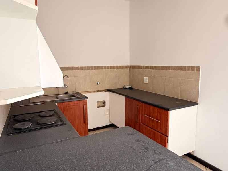 A dated kitchen featuring laminate countertops, built-in cabinetry, and an electric hob, currently requiring repairs to the cabinetry and wall finishes.