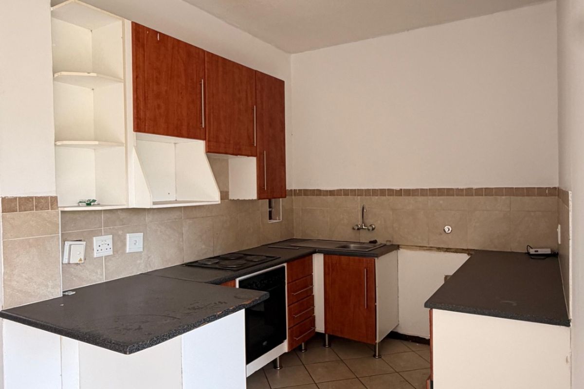A functional kitchen space featuring built-in cabinetry, tiled backsplash, and ceramic flooring, currently vacant and ready for renovation or modernization.