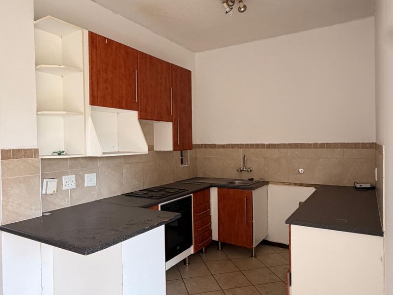 A functional kitchen space featuring built-in cabinetry, tiled backsplash, and ceramic flooring, currently vacant and ready for renovation or modernization.