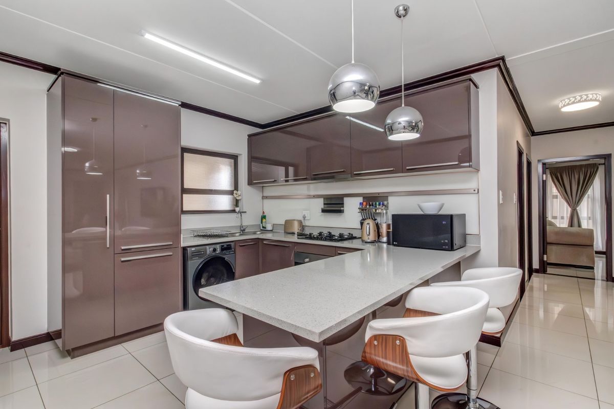 Modern kitchen featuring high-gloss cabinetry, stone countertops, a breakfast bar, integrated appliances, and tiled flooring with contemporary pendant lighting.