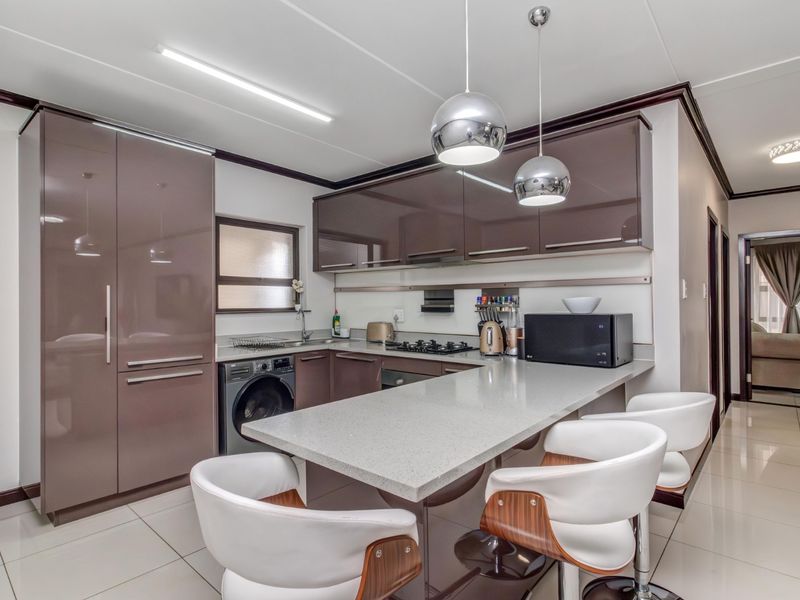 Modern kitchen featuring high-gloss cabinetry, stone countertops, a breakfast bar, integrated appliances, and tiled flooring with contemporary pendant lighting.