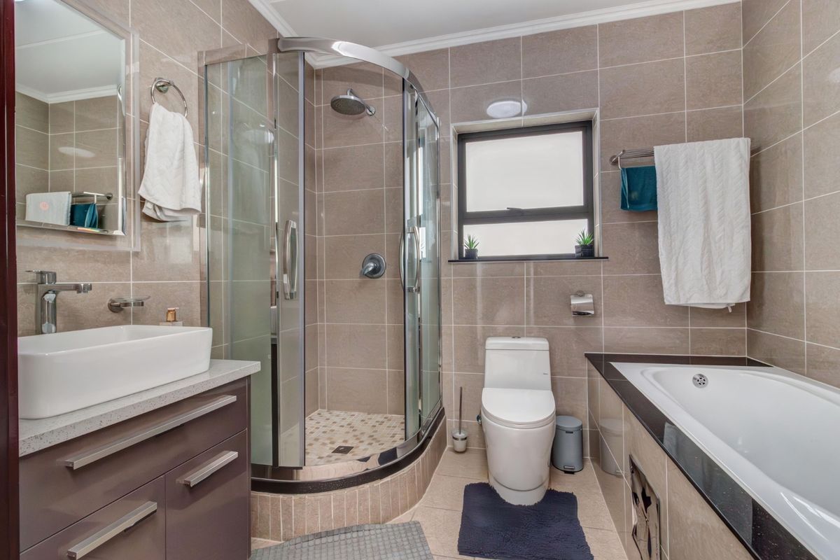 Modern bathroom featuring a glass shower enclosure, built-in bathtub, vanity with vessel sink, and neutral floor-to-ceiling tiling.