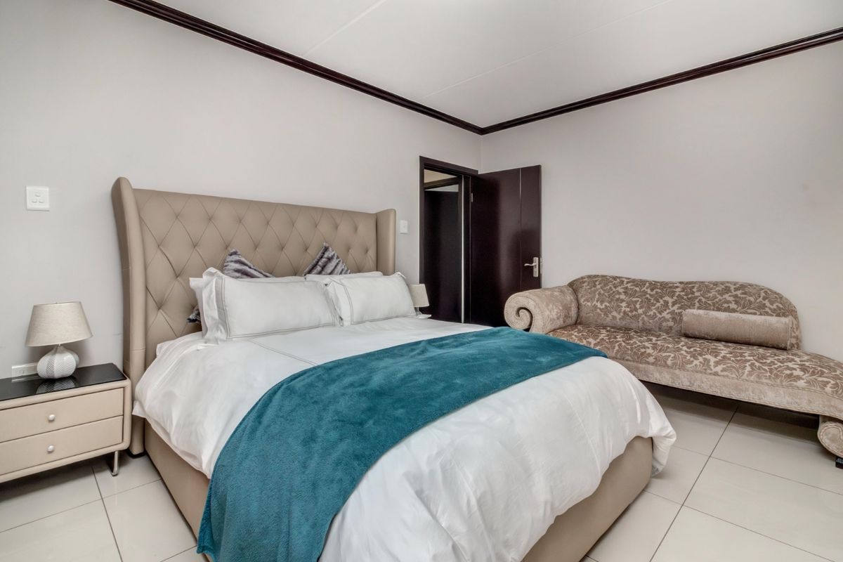 A well-maintained bedroom featuring neutral tiled flooring, dark wood door frames, and decorative crown molding.