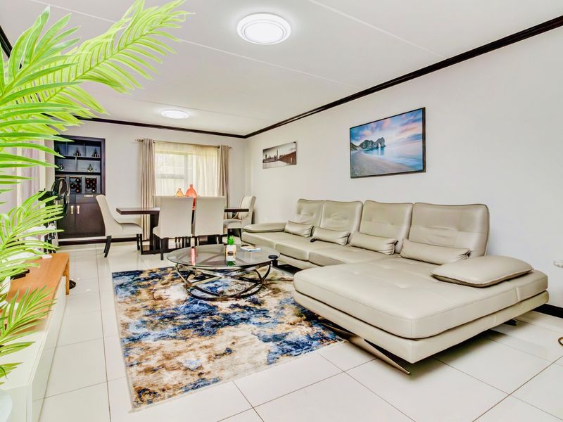 A spacious open-plan living and dining area featuring neutral tiled flooring, modern flush mount lighting, and a built-in wine storage unit.