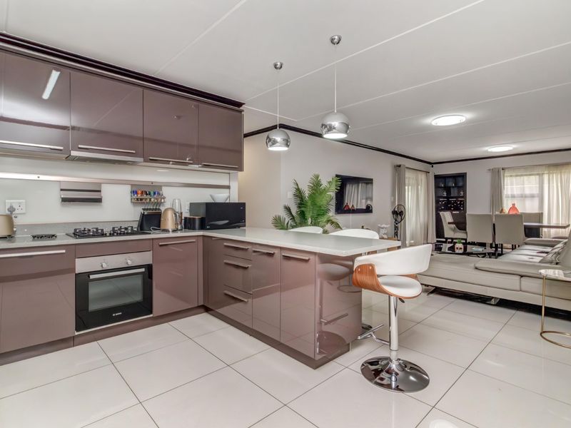 Modern open-plan kitchen and living area featuring high-gloss cabinetry, integrated appliances, stone countertops, and sleek tiled flooring throughout the space.