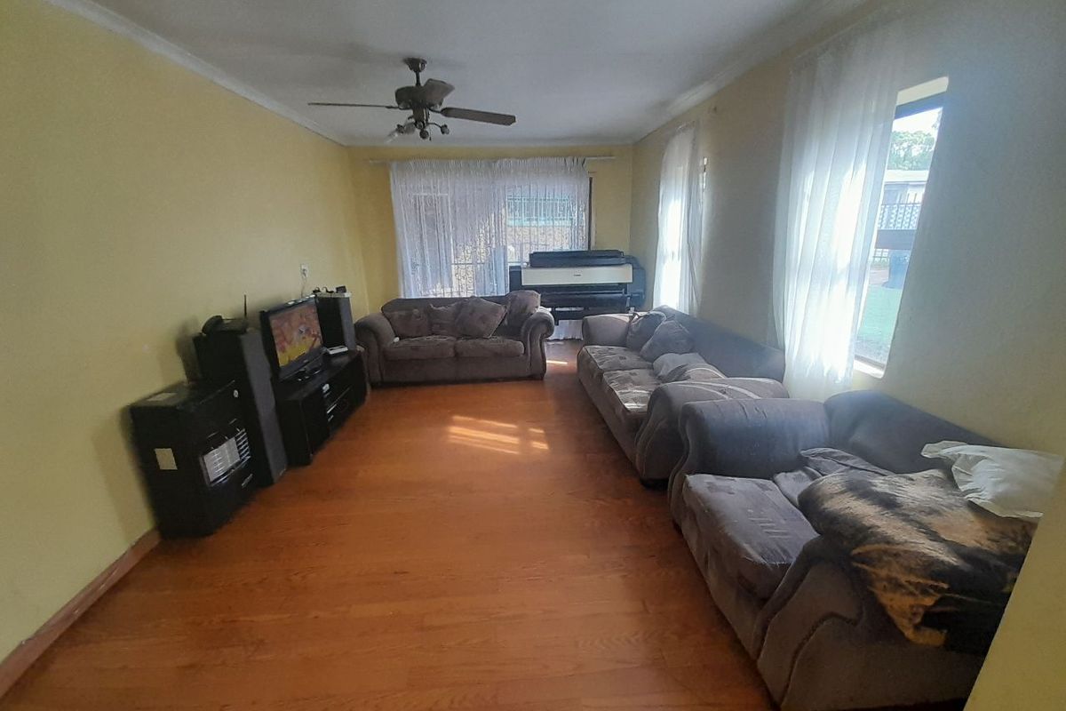 A spacious living room featuring hardwood flooring, a ceiling fan, and coved ceiling details, offering a comfortable and functional layout.
