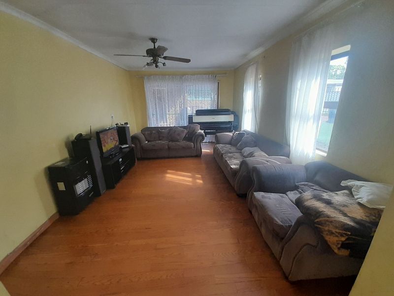 A spacious living room featuring hardwood flooring, a ceiling fan, and coved ceiling details, offering a comfortable and functional layout.