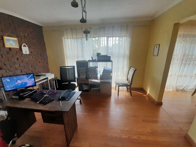 A home office space featuring laminate flooring and an exposed brick feature wall, providing a functional workspace with natural light.