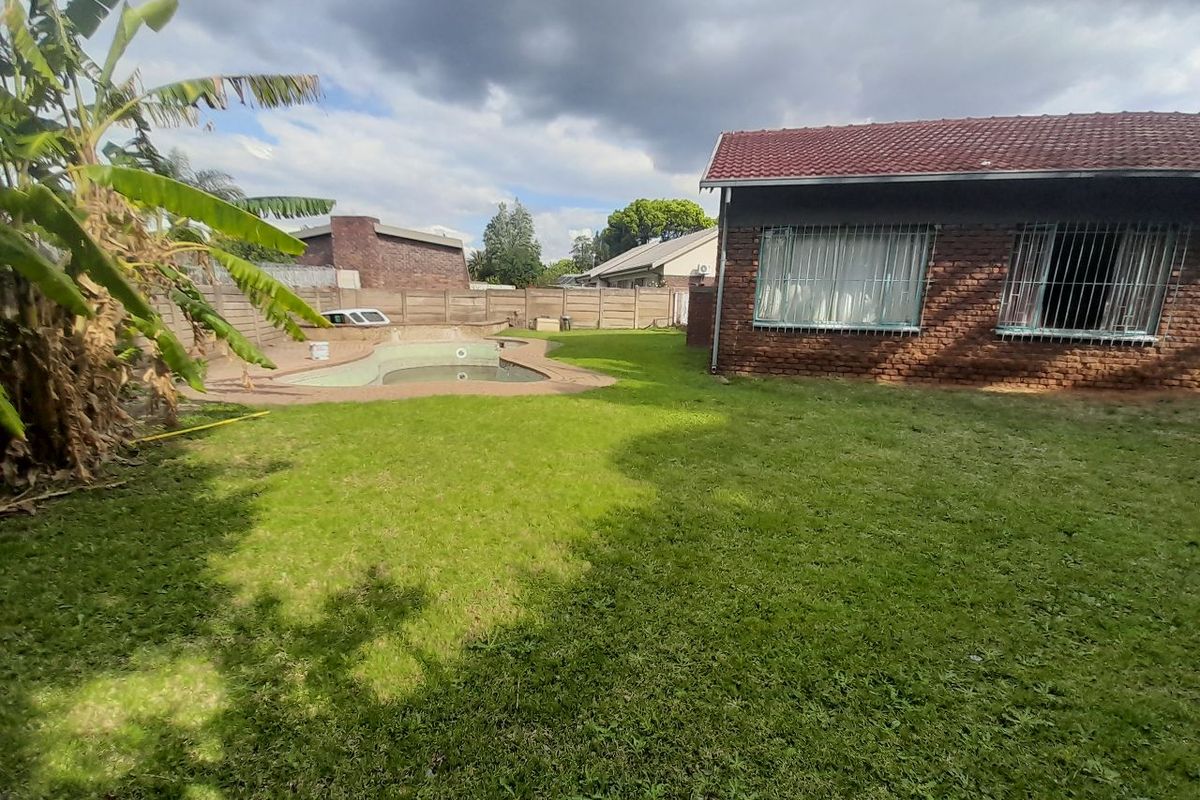 Rear garden featuring a swimming pool, paved surround, and brick boundary wall, adjacent to the main house with tiled roof and security bars.