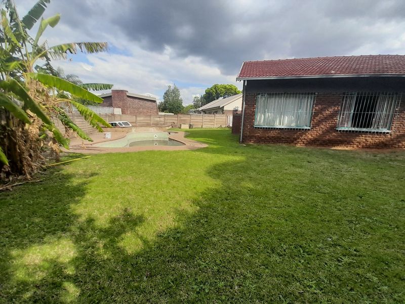 Rear garden featuring a swimming pool, paved surround, and brick boundary wall, adjacent to the main house with tiled roof and security bars.