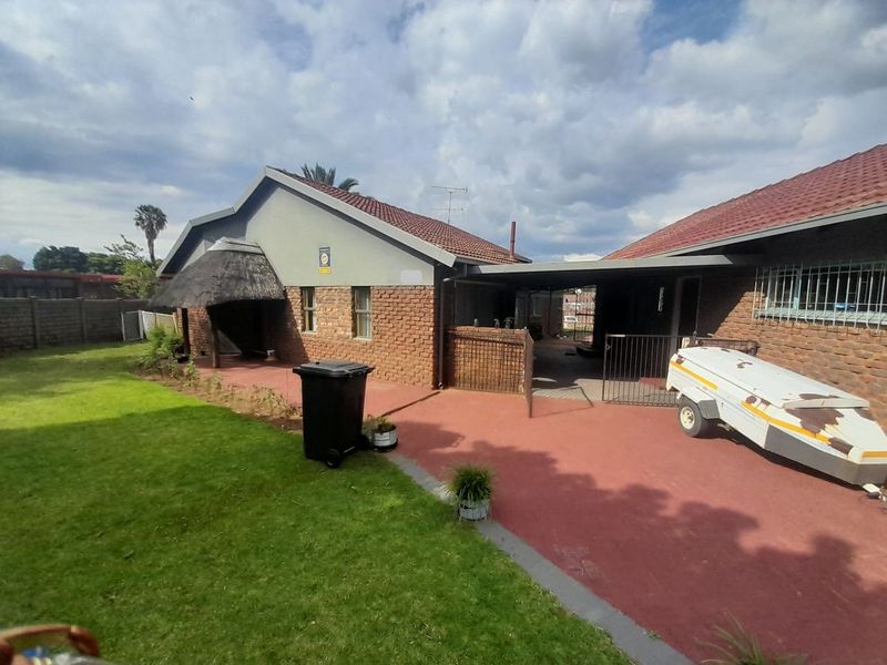 Rear view of the property featuring a brick facade, a covered patio area, a thatched roof section, and a paved driveway leading to the house.