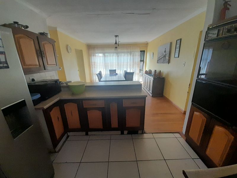 Open plan kitchen and dining area featuring dated cabinetry, a breakfast counter, and a mix of tiled and laminate flooring.