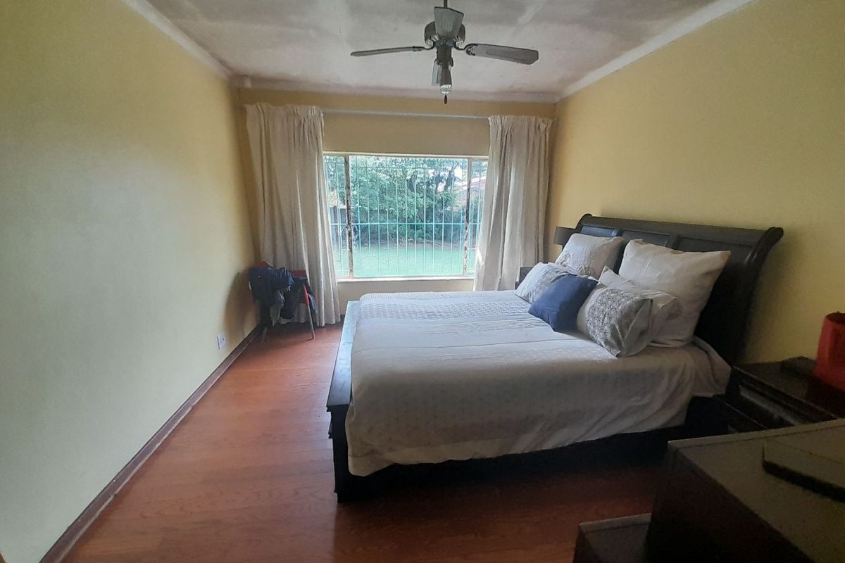 A bedroom featuring laminate flooring, a ceiling fan, and a window with security bars, currently requiring cosmetic updates to the walls and ceiling.