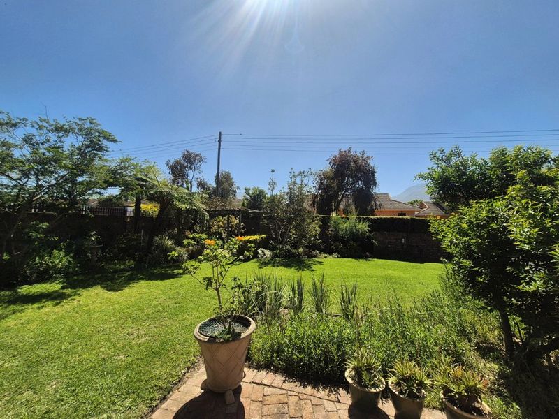 A well-maintained private garden featuring a lush green lawn, established trees, and brick-paved patio area.