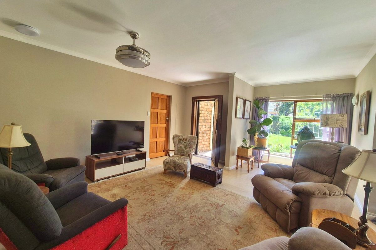 A comfortable living room featuring laminate flooring, a ceiling fan, and large windows providing natural light and garden access.
