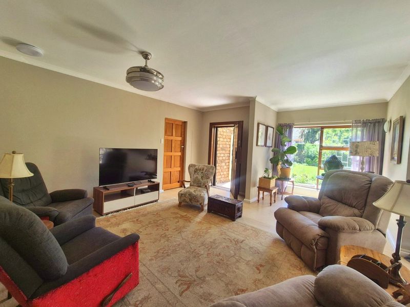 A comfortable living room featuring laminate flooring, a ceiling fan, and large windows providing natural light and garden access.